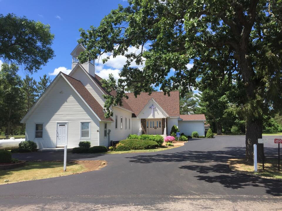 White country church with steeple and trees at Saint John Lutheran Church in Adams, Wisconsin, viewed from the drive.
