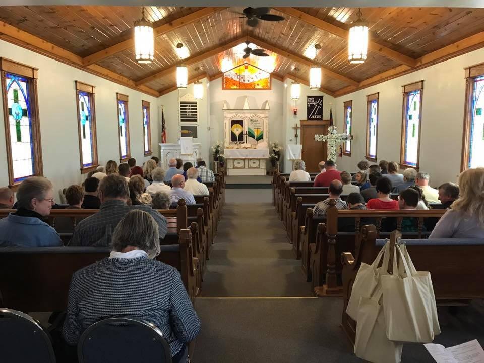 Congregation seated in the sanctuary at Saint John Lutheran Church in Adams, WI, facing the altar with stained-glass windows on both sides.